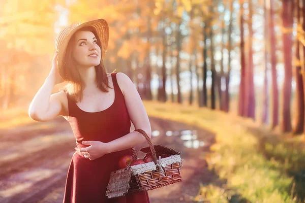 A girl in a hat on a walk in the park. A girl with a basket walks in autumn. Girl is walking along the road at sunset.