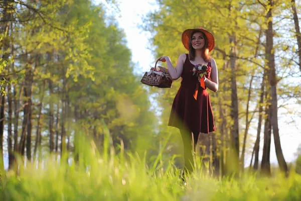 Een meisje in een hoed op een wandeling in het park. Een meisje met een mand-wandeling — Stockfoto