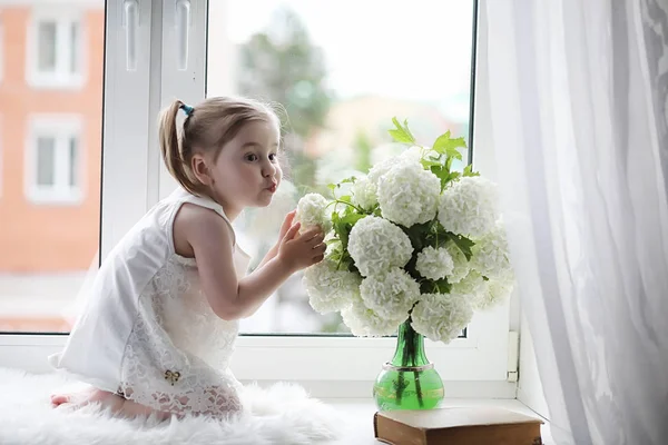 A little girl is sitting on the windowsill. A bouquet of flowers — Stock Photo, Image