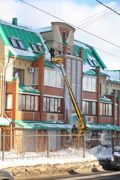 The cleaning service cleans the snow from the roof of the house.