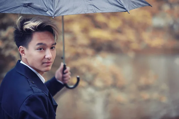 Otoño tiempo lluvioso y un joven con un paraguas — Foto de Stock