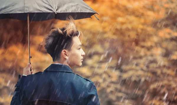 Autumn rainy weather and a young man with an umbrella — Stock Photo, Image