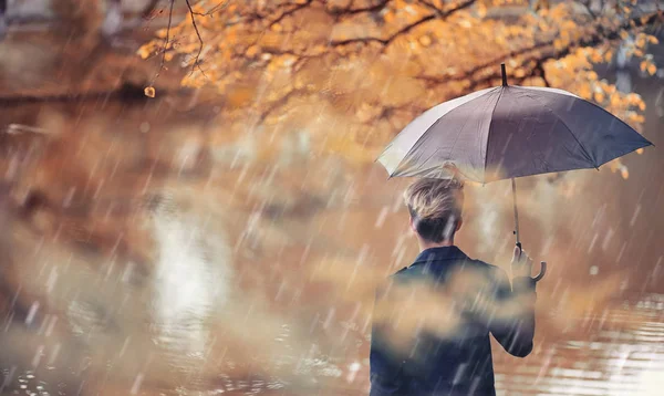 Herbstliches Regenwetter und ein junger Mann mit Regenschirm — Stockfoto