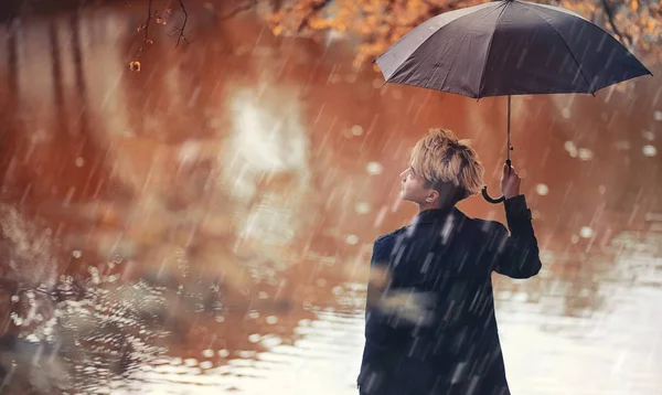 Herbstliches Regenwetter und ein junger Mann mit Regenschirm — Stockfoto