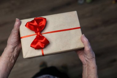 Büyükanne ellerinde kırmızı fiyonklu hediye kutusu