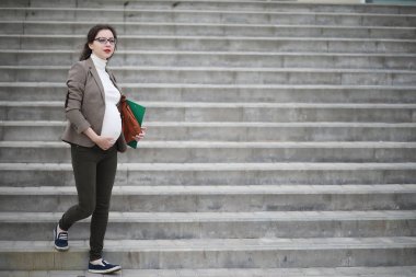 Hamile kadın binanın yakınındaki caddede telefonla konuşuyor.