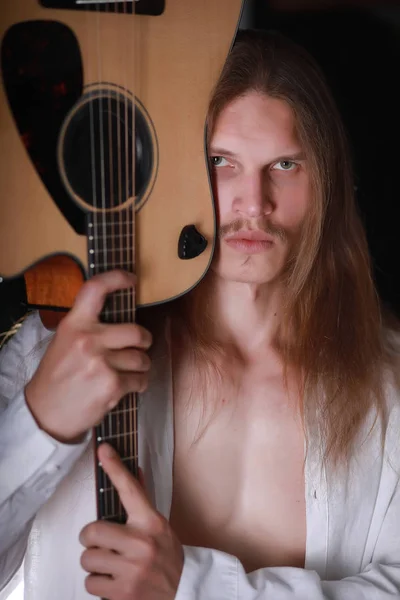 Молодой человек с длинными волосами и гитарой — стоковое фото