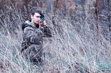 Kamuflaj ve bir sp üzerinde bir ormanda bir av tüfeği ile bir adam