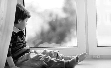 Küçük çocuk bir kitap okuyor. Çocuğun pencerenin önünde oturur bir