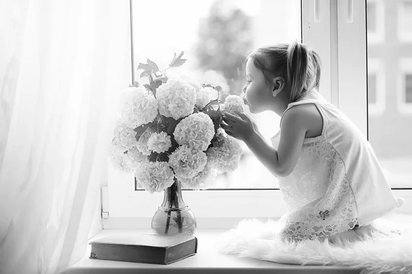 Una niña está sentada en el alféizar de la ventana. Un ramo de flores —  Fotos de Stock