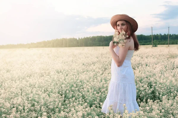 Beyaz elbiseli kız sarı çiçekli bir tarlada çiçek açıyor. — Stok fotoğraf