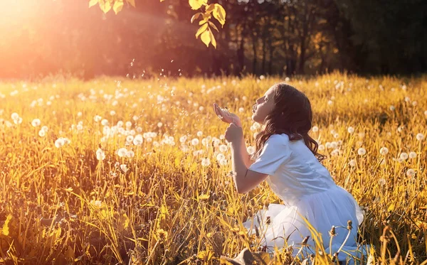 Adolescente soplando semillas de una flor de diente de león en un parque — Foto de Stock