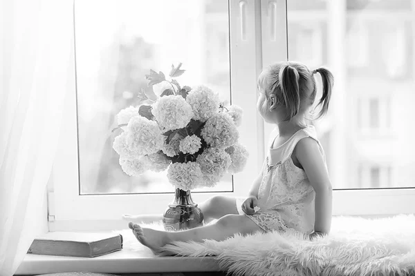 Una niña está sentada en el alféizar de la ventana. Un ramo de flores —  Fotos de Stock