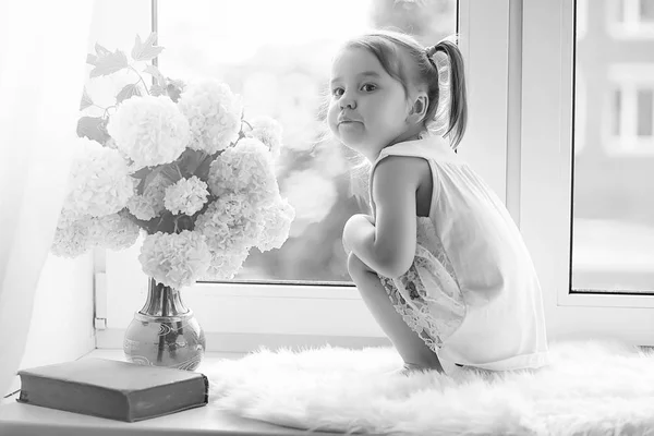 A little girl is sitting on the windowsill. A bouquet of flowers — Stock Photo, Image