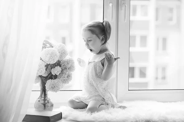 Una niña está sentada en el alféizar de la ventana. Un ramo de flores —  Fotos de Stock