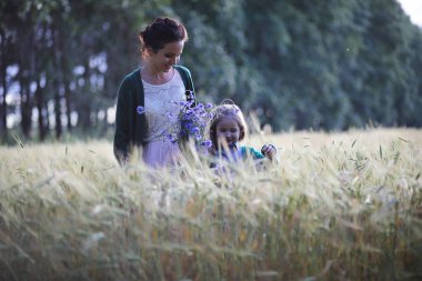 Genç anne yürüyerek buğday alanları içerisinde