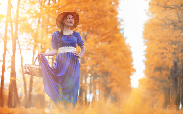 Young beautiful girl in dresses on nature. A girl in a hat walks in the park. Young woman on picnic with a basket outside the city.
