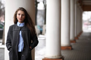 Genç, güzel bir kız, elinde bir sütunla binanın yanında yürüyor.