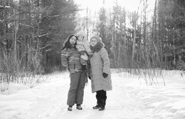 Siyah beyaz bir fotoğraf. Kışın elinde çocuğu tutan bir ebeveynin fotoğrafı.