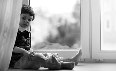 Küçük çocuk bir kitap okuyor. Çocuğun pencerenin önünde oturur bir