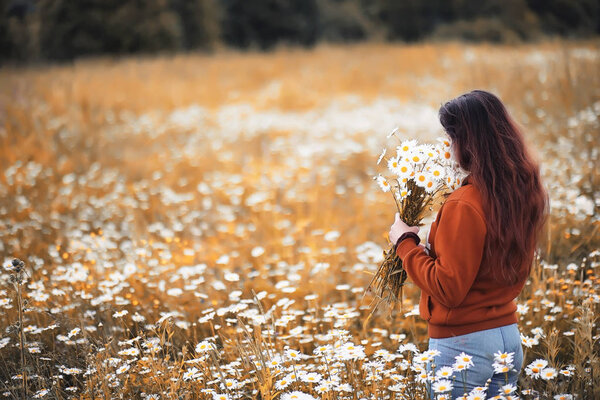 Beautiful girl collects daisies in autumn field eveninig sunset