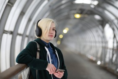 Young girl listens to music in big headphones in the subway clipart