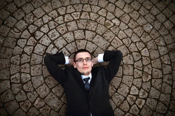 Un uomo in giacca e cravatta giace sul pavimento di mattoni — Foto Stock