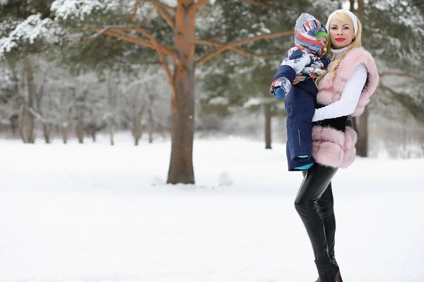 Jovem mãe caminha em um dia de inverno com um bebê em seus braços em th — Fotografia de Stock