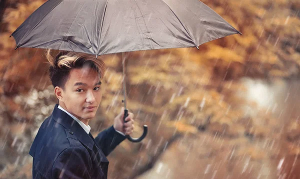 Herbstliches Regenwetter und ein junger Mann mit Regenschirm — Stockfoto