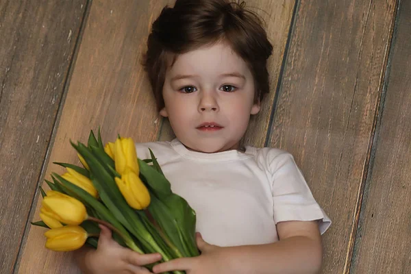 Un niño pequeño con un ramo de tulipanes amarillos. Un chico con un regalo — Foto de Stock