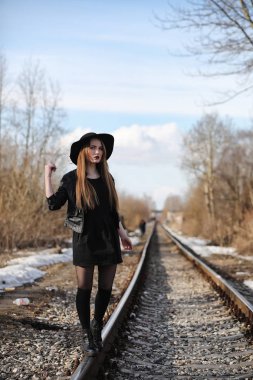 Şapkalı ve dışarıda siyah makyajlı güzel bir kız. Sokakta Gotik tarzında bir kız. Şehir caddesinde bir kız yürüyor. Deri yelekli ve telefonlu.