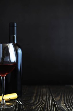 Masada bir bardak kırmızı şarap. Siyah şişe ve bir bardak şarap..