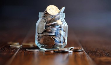 Ahşap bir zemindeki cam kavanozdaki bozuk paralar. Bankadaki bozukluklardan gelen cep tasarrufları. İçinde bozuk paralar olan cam bir kavanozda kumbara..