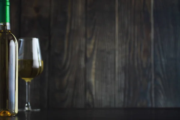 Transparent bottle of white dry wine on the table. White wine glass on a wooden wall background.