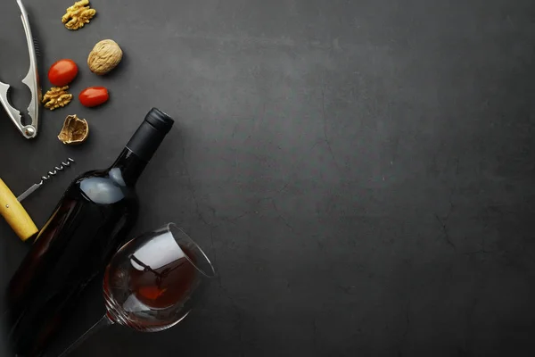 Red wine on a stone background. Wine glass and black wine bottle. Nuts cheese and tomatoes for snack.