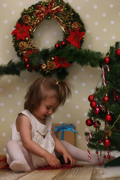 Little girl sitting in front of a Christmas tree — Stock Photo, Image