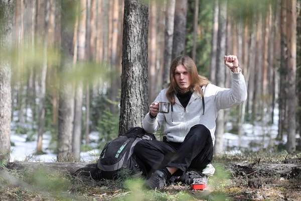 A man in a campaign drinks tea. A young traveler in the woods ca