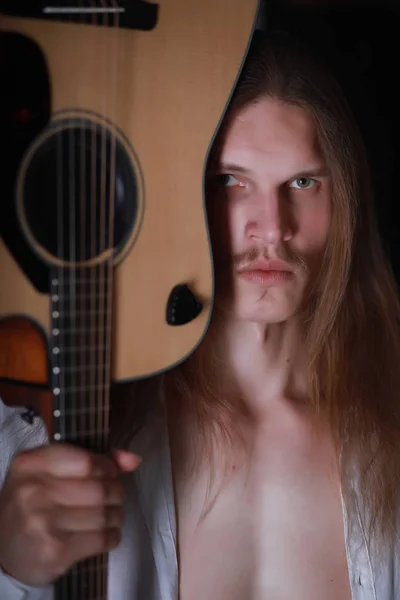 Молодой человек с длинными волосами и гитарой — стоковое фото