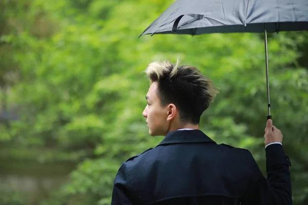 Bahar yağmurlu hava ve bir şemsiye ile genç bir adam — Stok fotoğraf