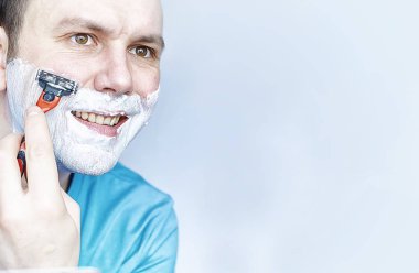 Bir adam aynanın önünde tıraş olur. Tıraş köpüğü. Tek kullanımlık jilet..