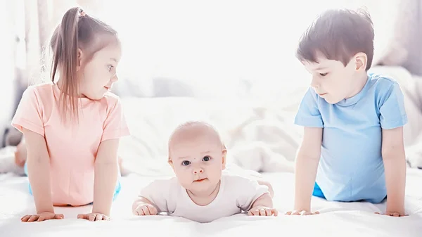 Kinder liegen auf dem Bett neben dem Neugeborenen, kleine Schwester. — Stockfoto