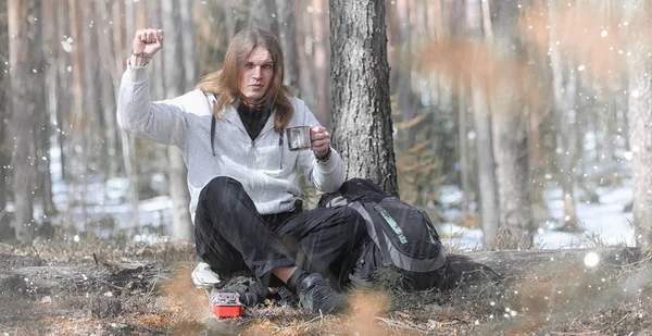 A man in a campaign drinks tea. A young traveler in the woods ca