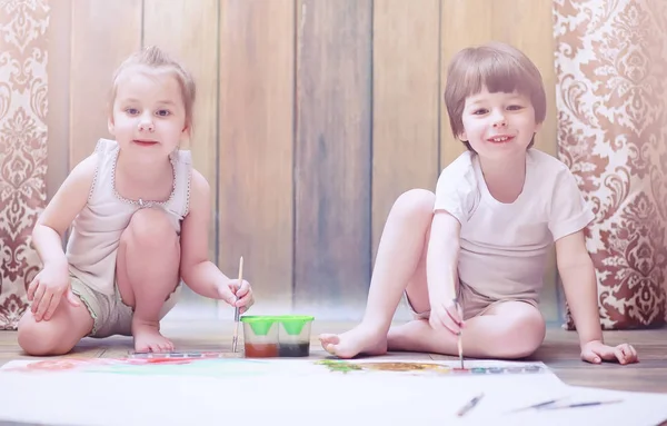 Niños pequeños pintan en una hoja grande de papel —  Fotos de Stock