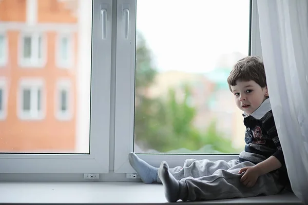 The little boy is reading a book. The child sits at the window a — Stock Photo, Image