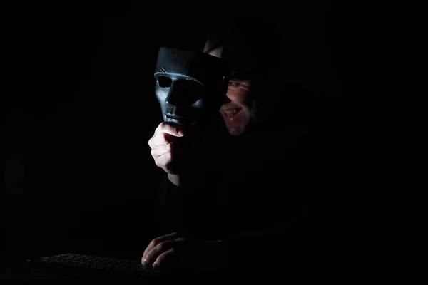 Un hombre con una máscara imprime en el teclado en la oscuridad — Foto de Stock