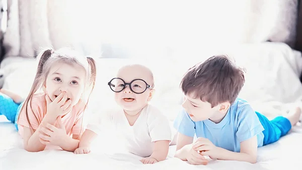 Children lie on the bed next to the newborn baby, little sister. — Stock Photo, Image