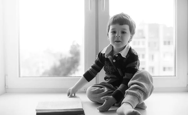 El niño está leyendo un libro. El niño se sienta en la ventana a —  Fotos de Stock