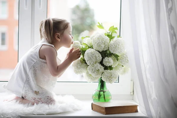 Küçük bir kız kenarında oturuyor. Bir buket çiçek — Stok fotoğraf