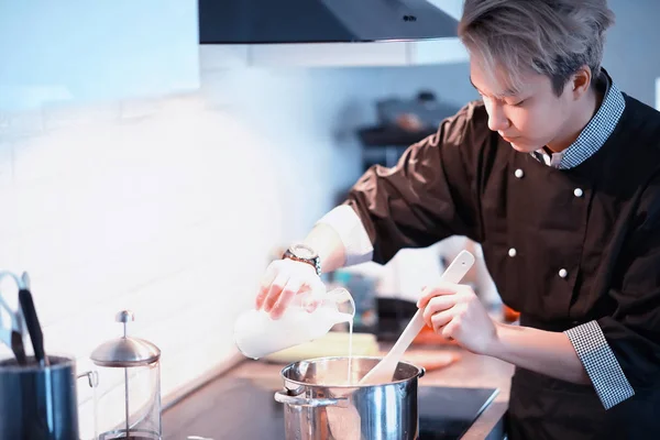 Asian cook in the kitchen prepares food in a cook suit