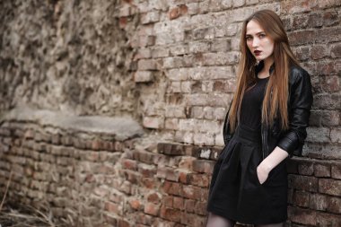 Şapkalı ve dışarıda siyah makyajlı güzel bir kız. Sokakta Gotik tarzında bir kız. Şehir caddesinde bir kız yürüyor. Deri yelekli ve telefonlu.